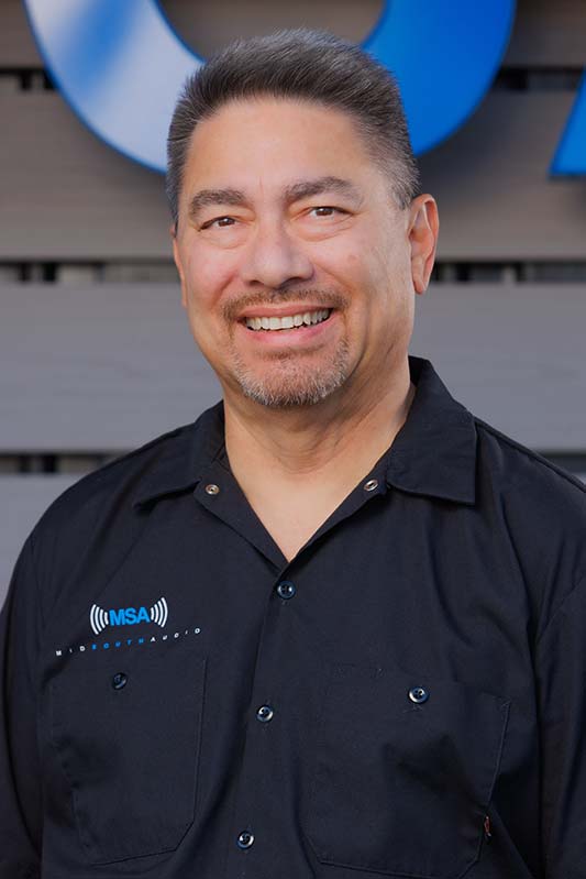Andy-Salita-01 Smiling man in a black MSA-branded polo shirt, standing outdoors in front of a blue backdrop with signage visible behind him.